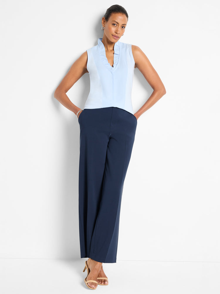 Sleeveless powder blue blouse with a frilled collar and fitted bodice worn above flowing navy wide-leg pants.