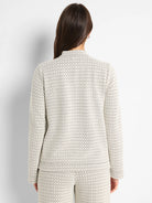 Cream knit top with subtle dark swirling pattern, mock neck, long sleeves, viewed from the back.
