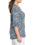 Knit top with repeating pattern of blue, black, & white dotted circles, bordered by brown shapes. Round neck, 3/4 sleeves.