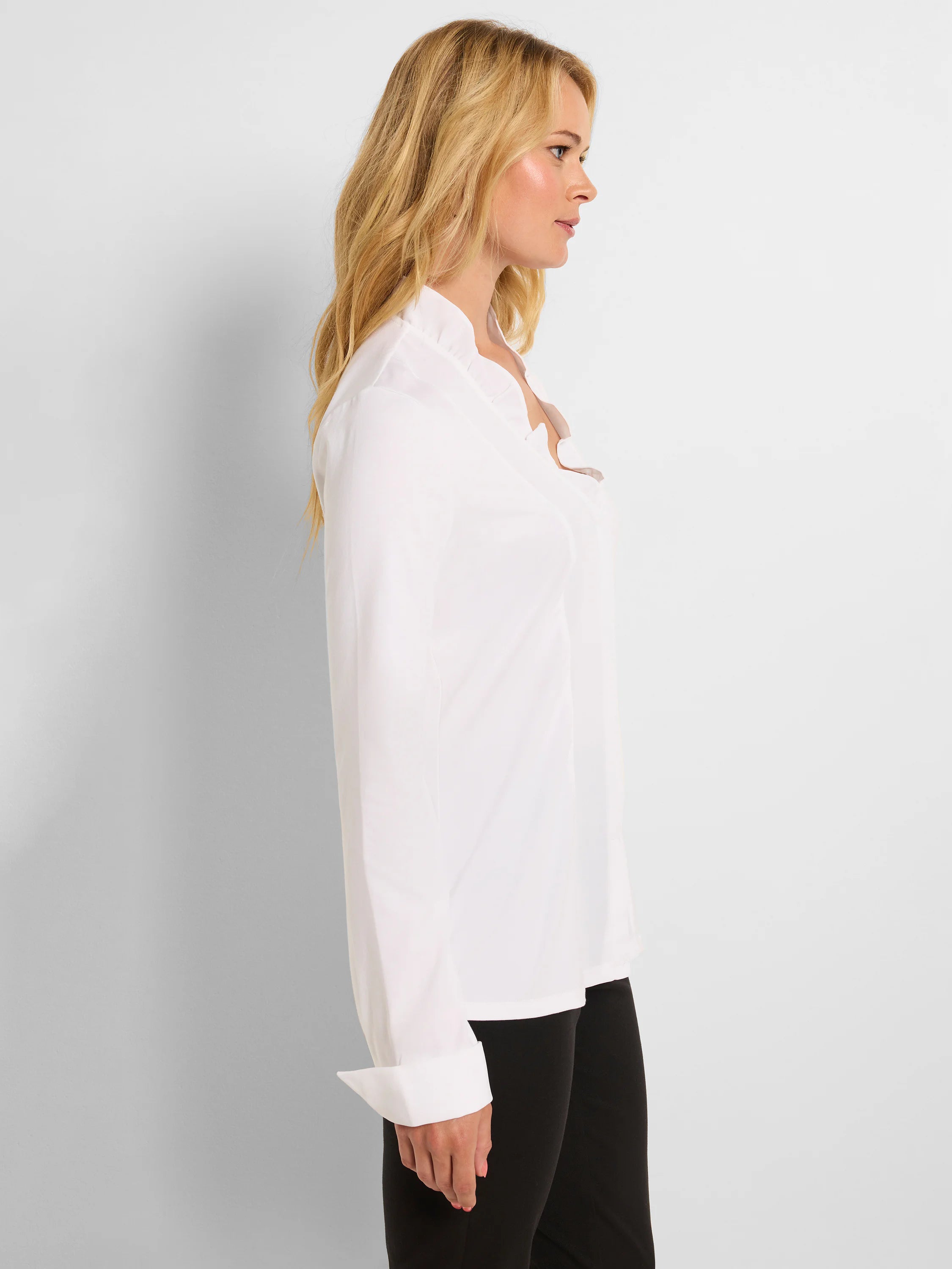 White shirt with a ruffled neckline, long sleeves, and cuffed wrists.
