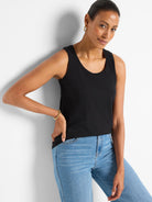 Black knit tank top with a scoop neck. Worn by a model paired with light blue jeans.