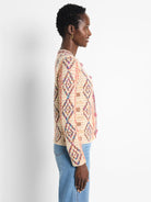 Cream knit jacket with variegated diamond pattern in red, blue, pink, brown; colorful pom-pom trim.