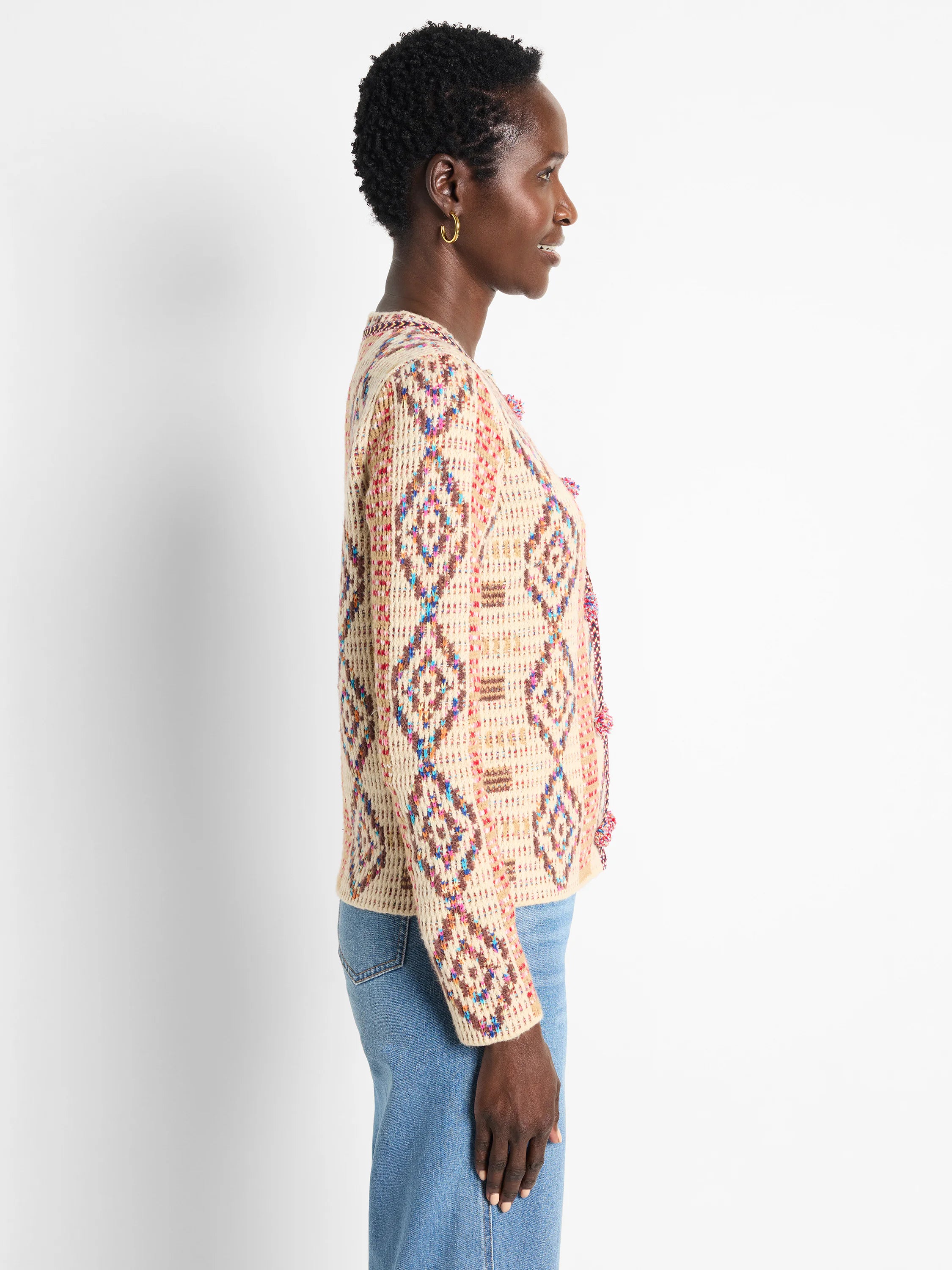 Cream knit jacket with variegated diamond pattern in red, blue, pink, brown; colorful pom-pom trim.