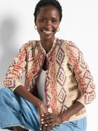 Knit jacket, beige base with multicolored geometric pattern in red, brown, and blue.  Pom-pom button details.