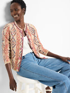 Cream knit jacket with multi-color geometric weave (red, blue, pink, brown), braided trim, and pom-pom buttons.