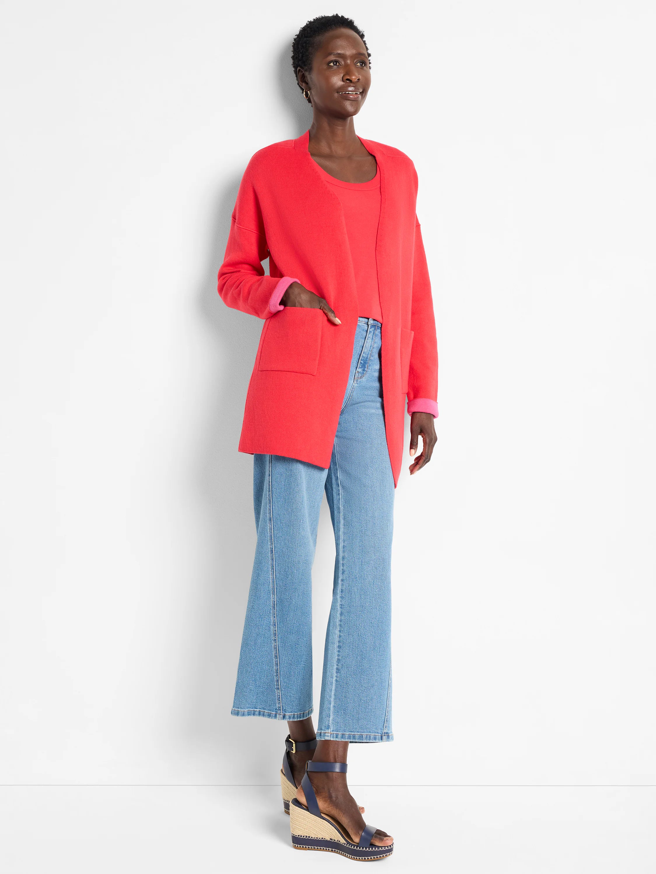 Red-orange open knit jacket with front pockets. Bright pink inner lining seen on reversible cuffs.