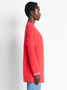 Coral knit jacket with bright pink folded cuffs, open front, and front pocket.