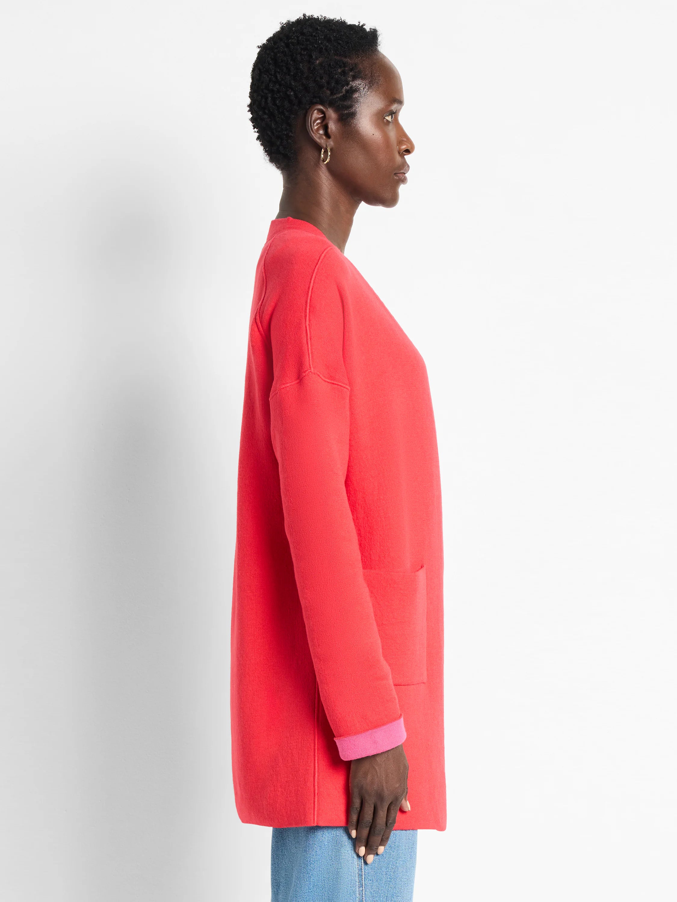 Coral knit jacket with bright pink folded cuffs, open front, and front pocket.