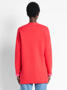 Back view of a coral knit jacket on a model. Long sleeves are cuffed to show a bright pink lining.