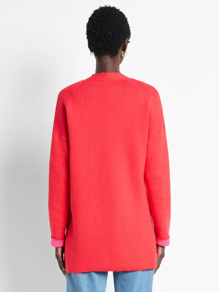 Back view of a coral knit jacket on a model. Long sleeves are cuffed to show a bright pink lining.