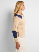 Beige knit sweater with navy blue organic "pebble" patches, visible stitching, and perforated details.