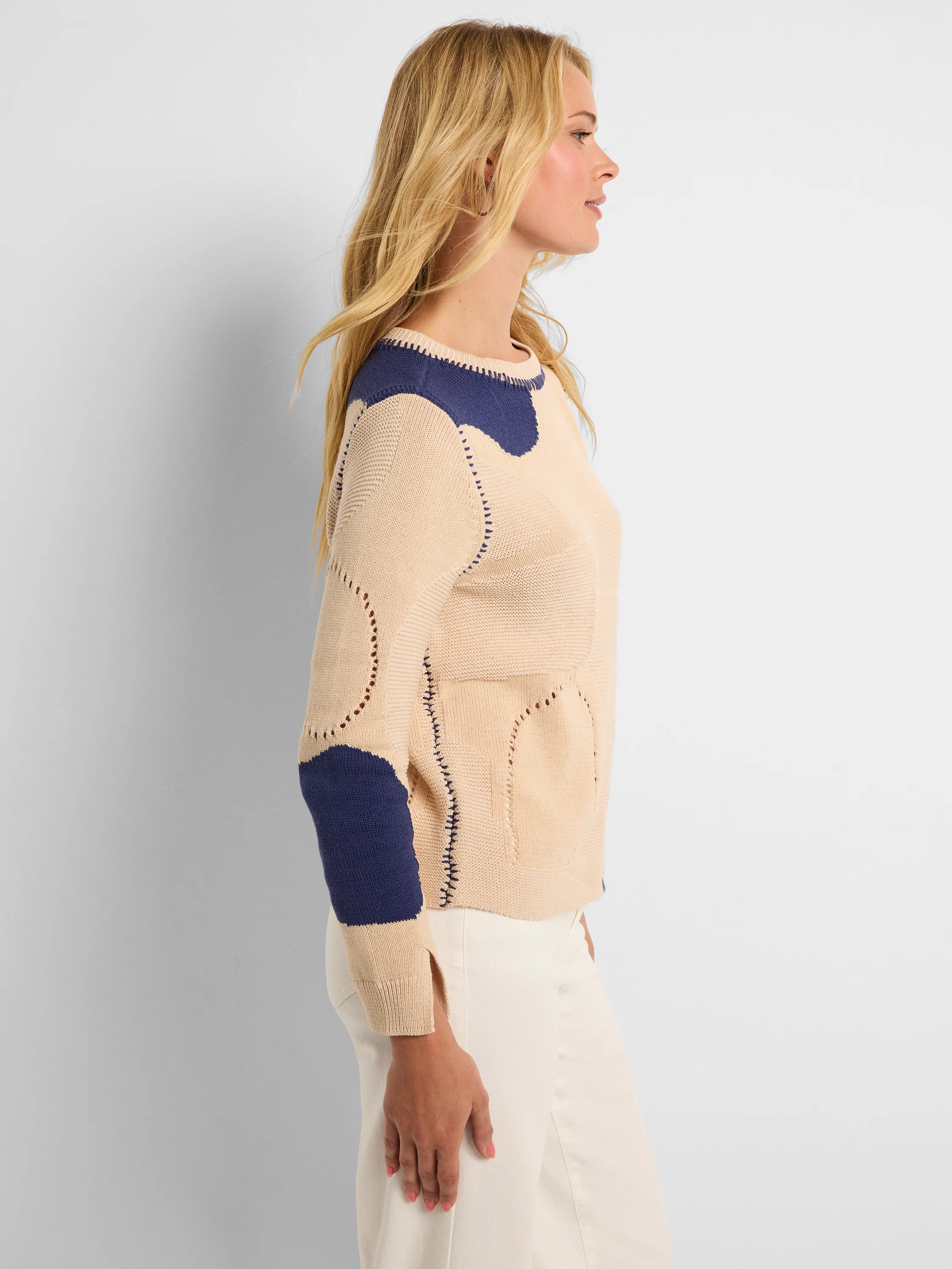 Beige knit sweater with navy blue organic "pebble" patches, visible stitching, and perforated details.