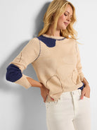Beige sweater with irregular navy patches, navy contrast stitching, and knitted pebble details with eyelets.