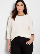 Off-white ribbed sweater with black and light-green trim at neckline and sleeves. Three-quarter sleeves.