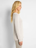 Ecru V-neck knit sweater worn by a model. Features long sleeves and ribbed cuffs and hem.
