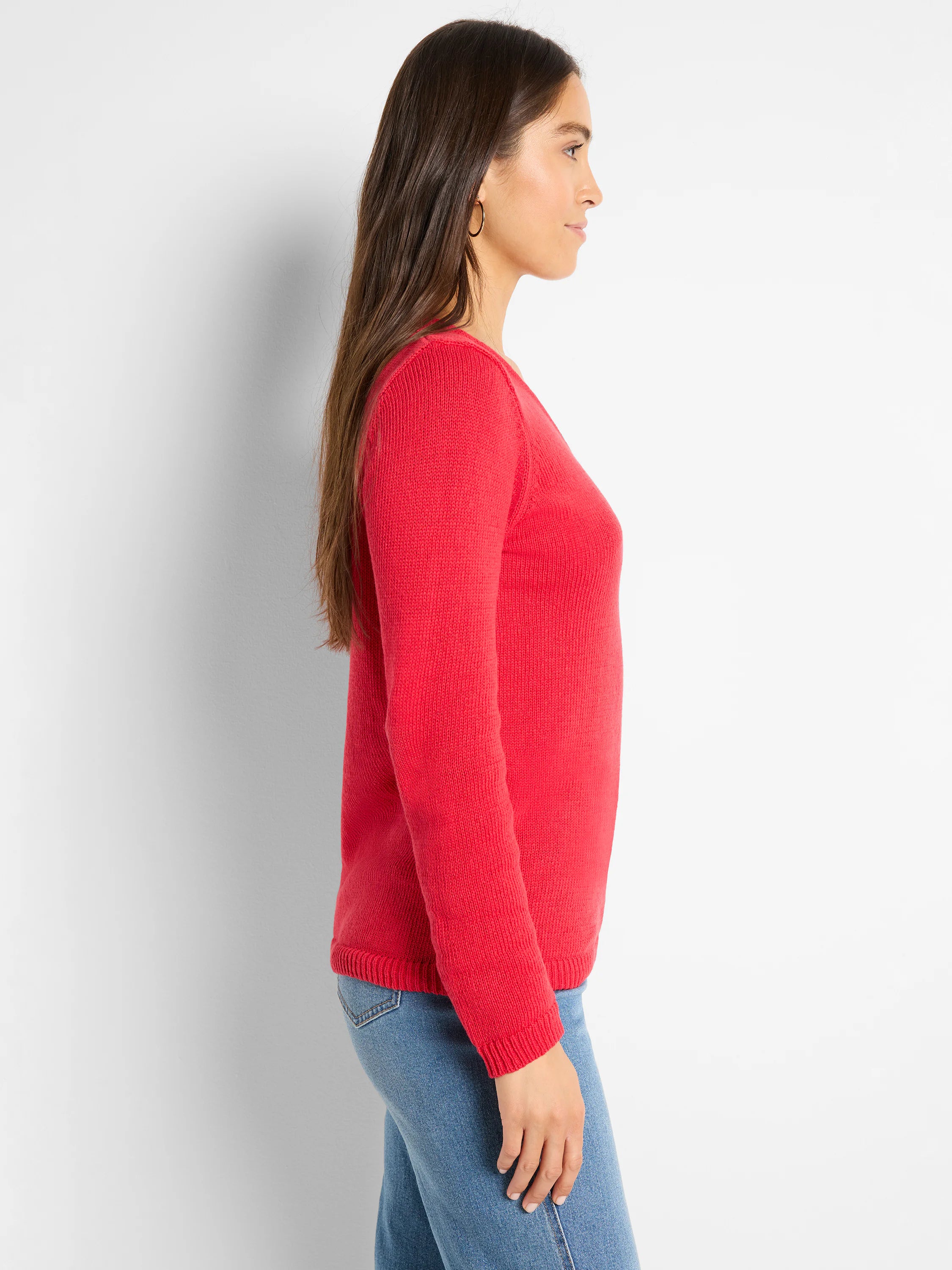 Red long-sleeve sweater with a fine knit texture and ribbed cuffs and hem, worn by a woman in profile.