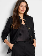 Black linen-cotton blazer with mandarin collar, three buttons, and pockets.  Model wears it with black top and trousers.
