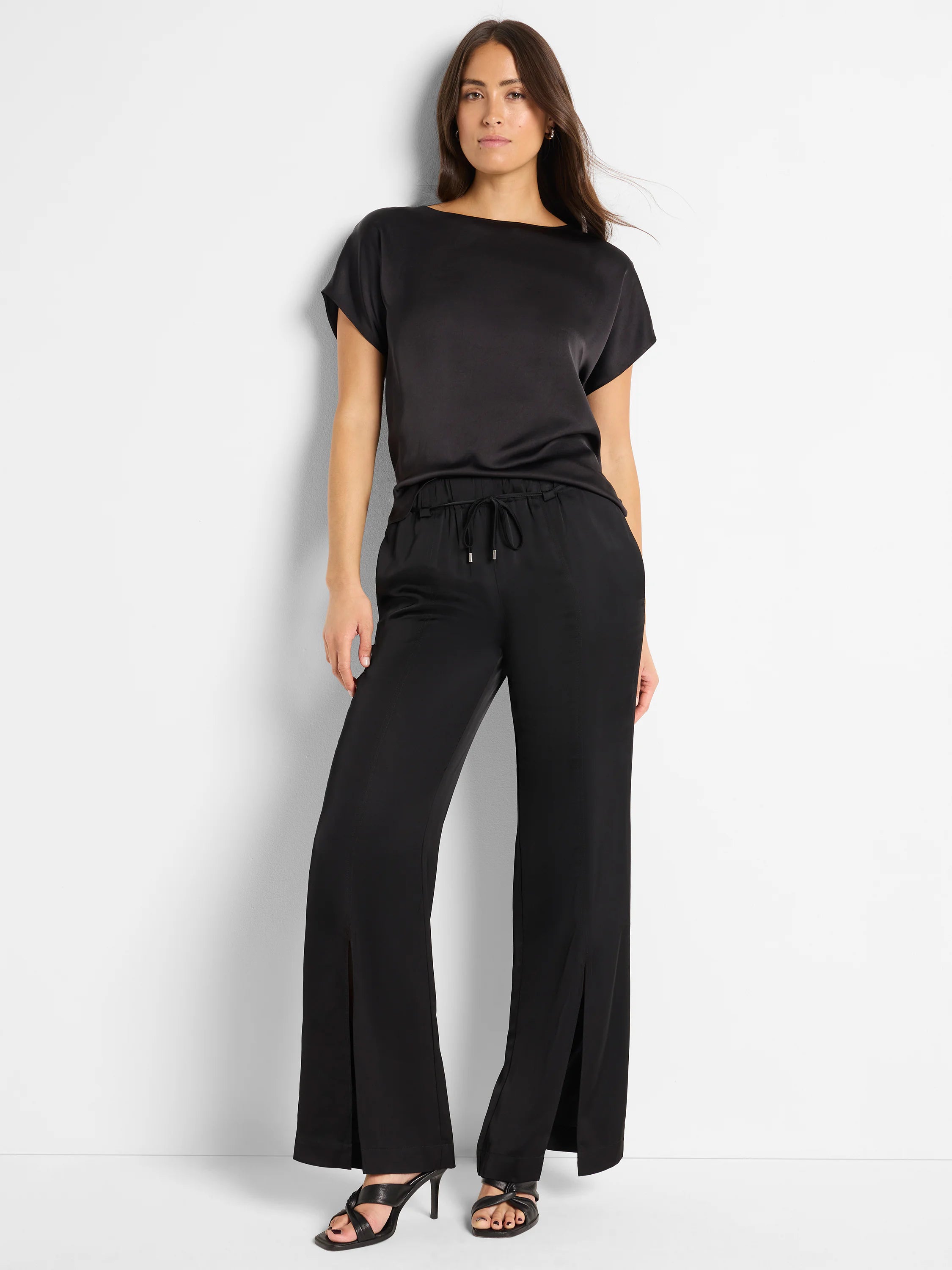 Black woven top with short sleeves and boat neck, paired with black wide-leg pants featuring side slits and drawstring waist.