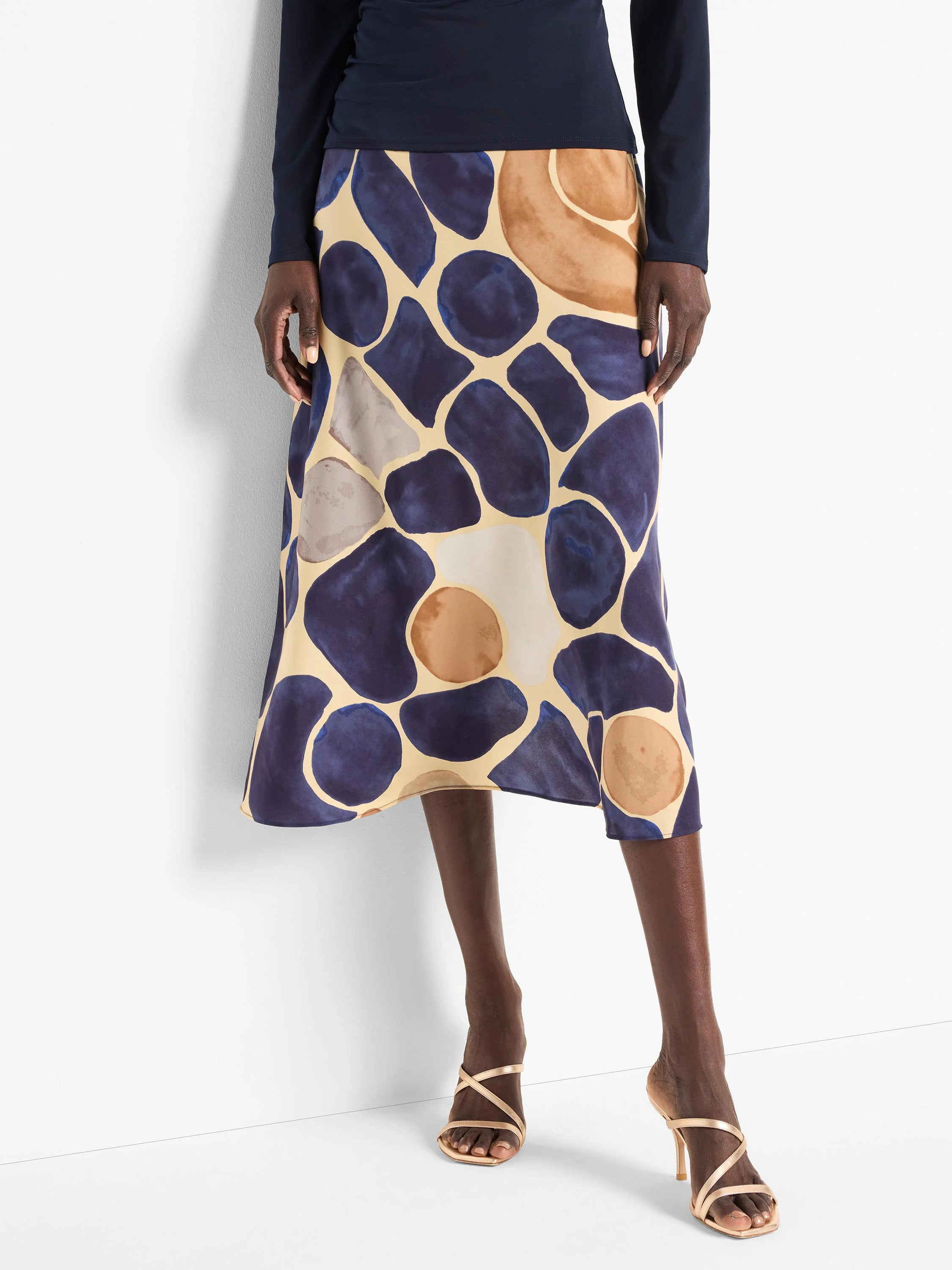 Mid-length slip skirt in beige with an abstract print of dark blue, taupe, and light brown pebble shapes.