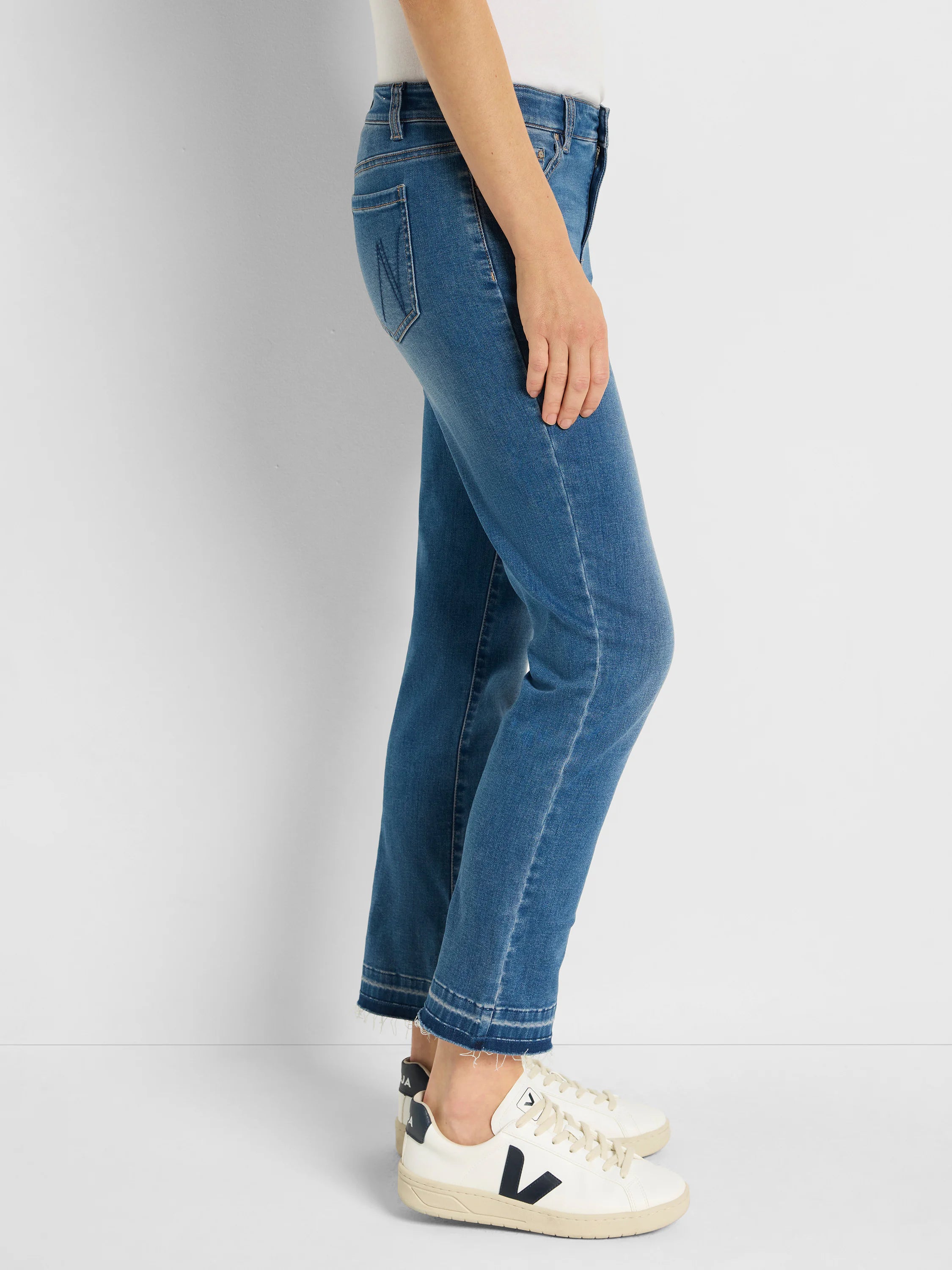 Medium blue straight leg jeans with a released, frayed hem. Worn on a person.