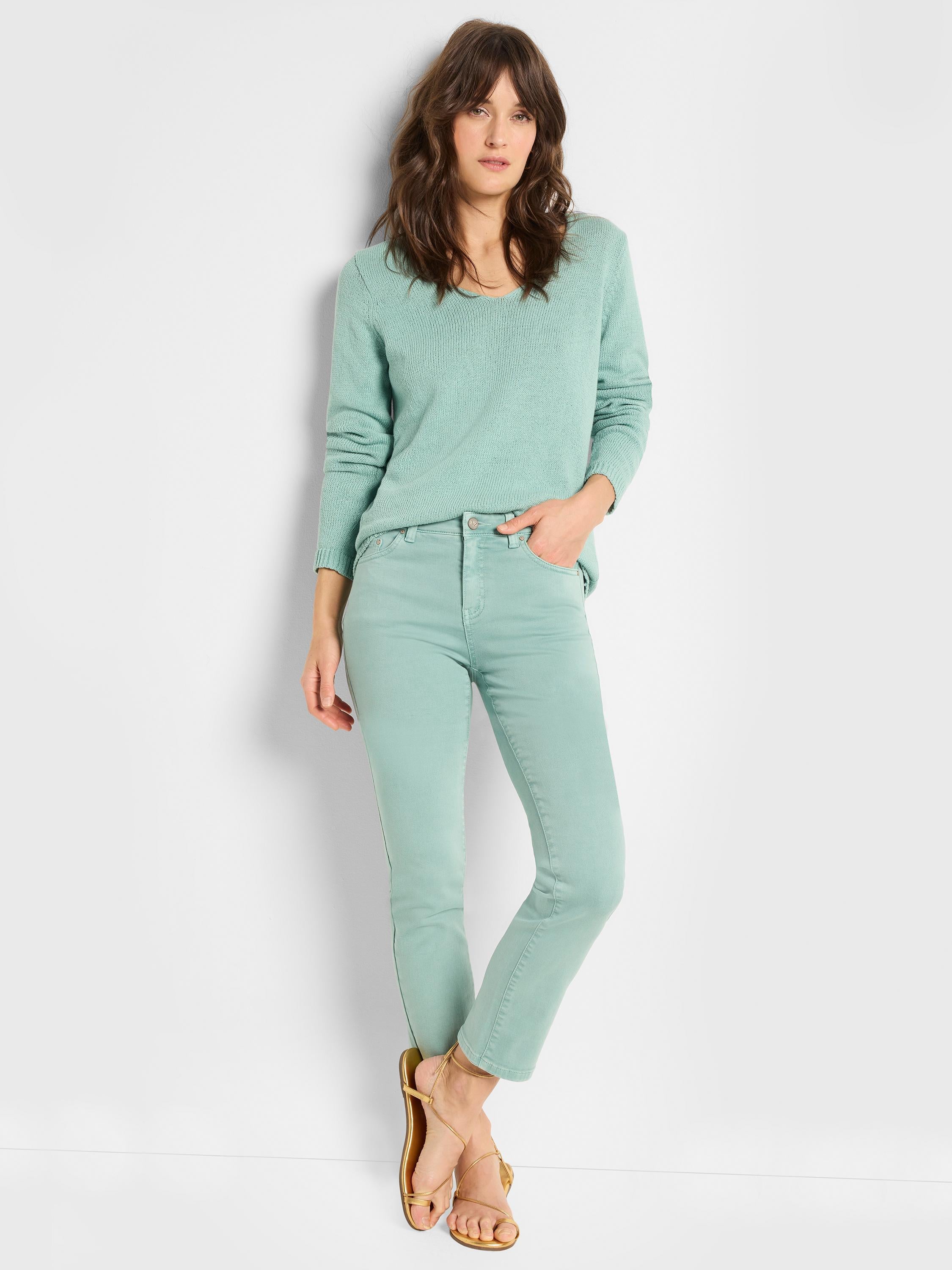 A model wears a relaxed mint green knit sweater and matching slim-fit ankle jeans.