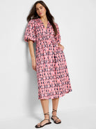 Midi dress in pink, coral, and navy blue Ikat pattern. Puff sleeves, V-neck, and fitted waist.