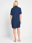 Navy blue collared dress, back view, on a model. Short cuffed sleeves, straight relaxed fit, above-knee length.