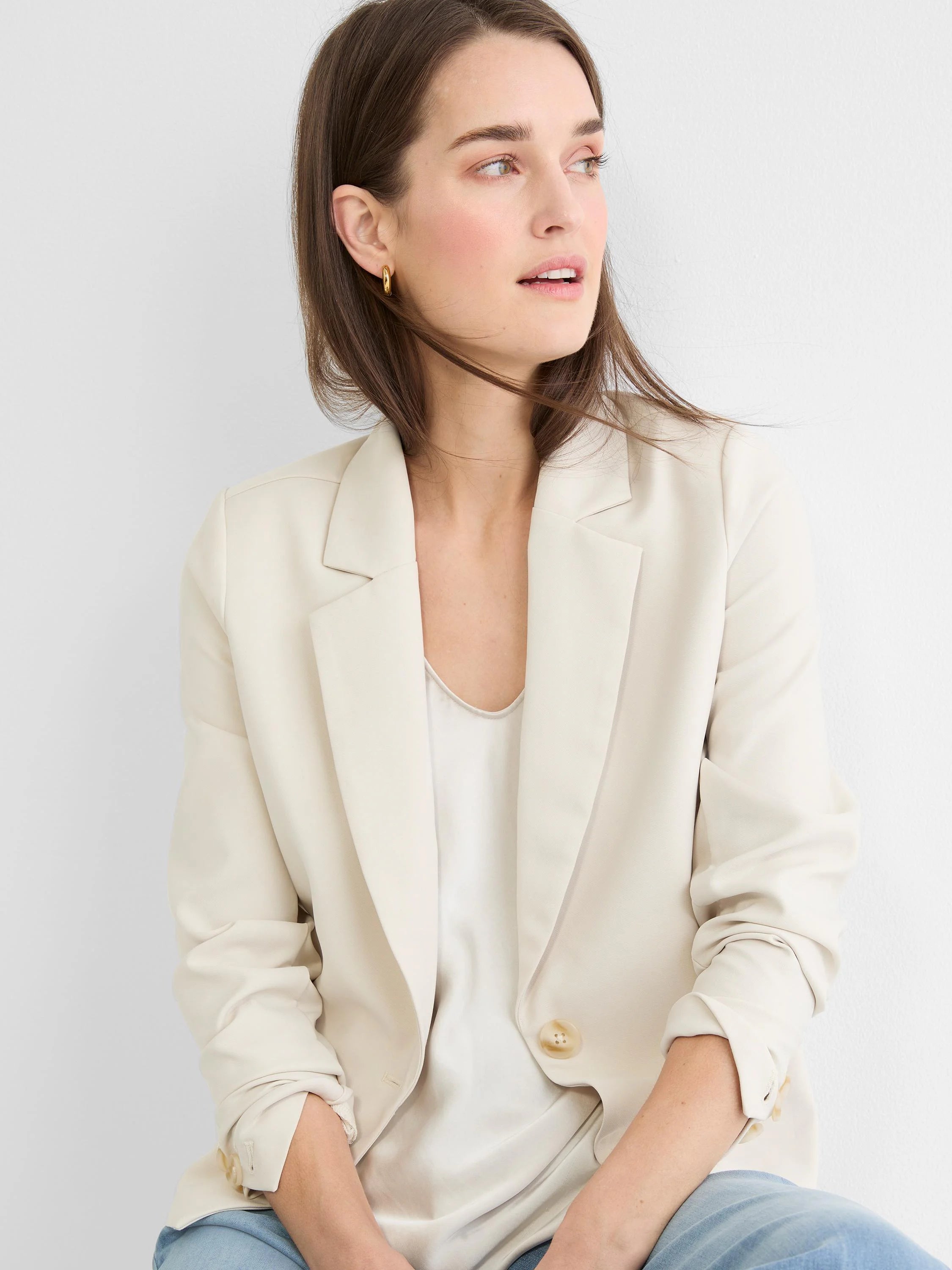 Model wears a cream single-button blazer with notched lapels. Sleeves casually pushed up, worn over a light top.