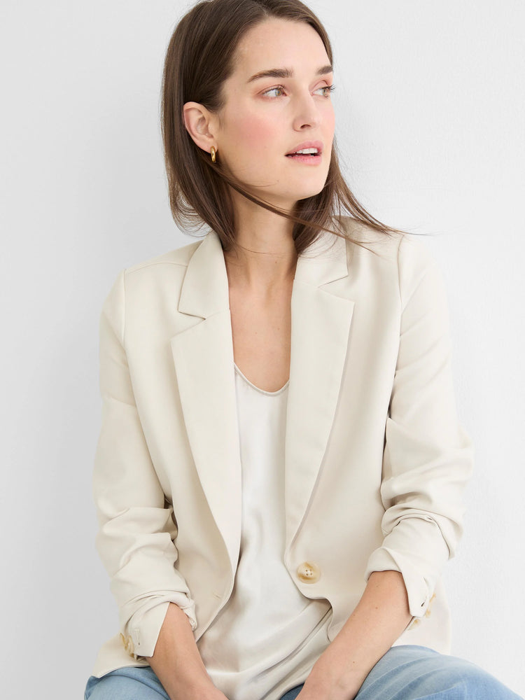 Model wears a cream single-button blazer with notched lapels. Sleeves casually pushed up, worn over a light top.
