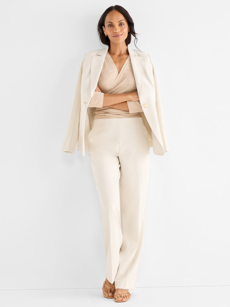 The model wears a sophisticated cream ensemble with a draped blazer, wide-leg trousers, and a beige knit wrap top.