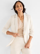 A fitted cream blazer with notched lapels and a single button is worn open over a wrapped metallic knit top.