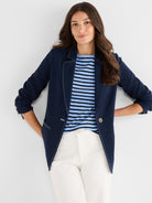 A tailored navy blazer featuring bold white contrast stitching along the lapels, seams, and pockets is worn open.