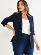 This navy blazer features white contrast stitching, a relaxed fit, and cuffed three-quarter sleeves, styled over a white tank.