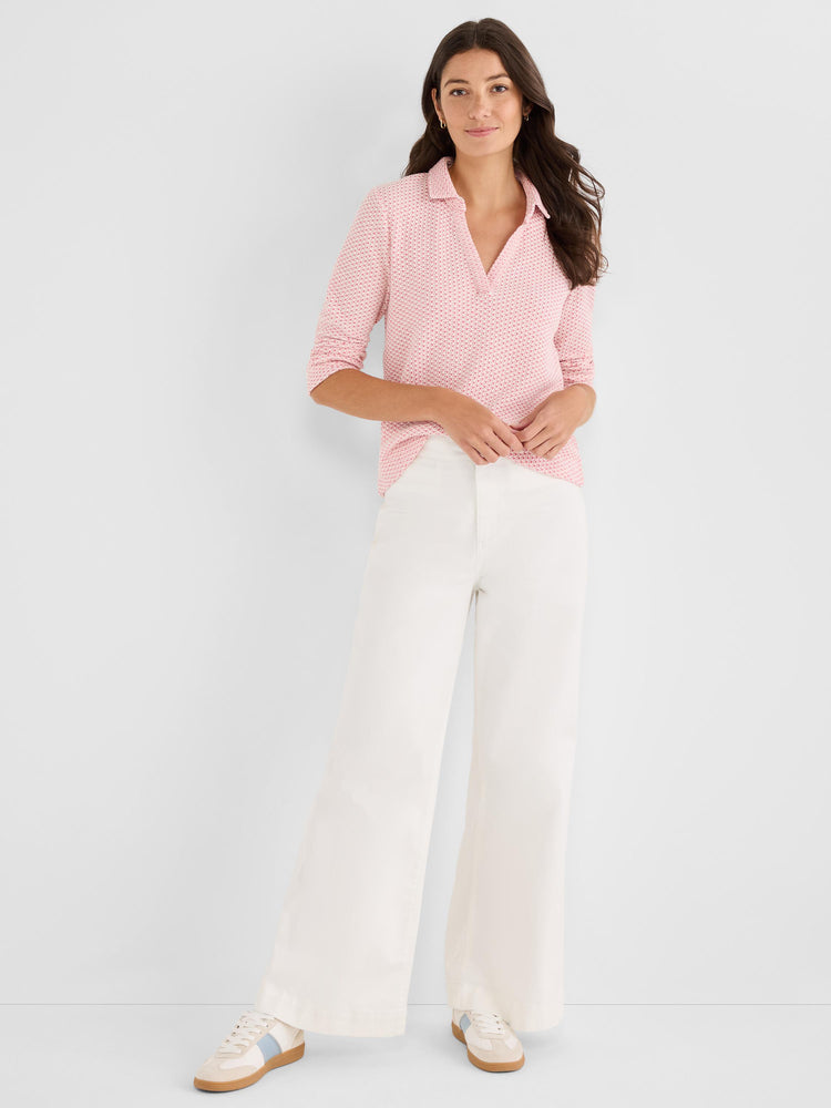 A model wears a relaxed pink patterned polo top with an open placket, paired with crisp, high-waisted white wide-leg trousers.