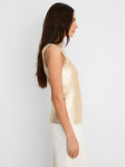 Sleeveless metallic gold ribbed tank top with a subtle sheen, worn by a model in profile.