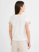 Ecru cotton slub tee with short sleeves featuring tan, ornate leaf embroidery along the hems. Model shown from back.