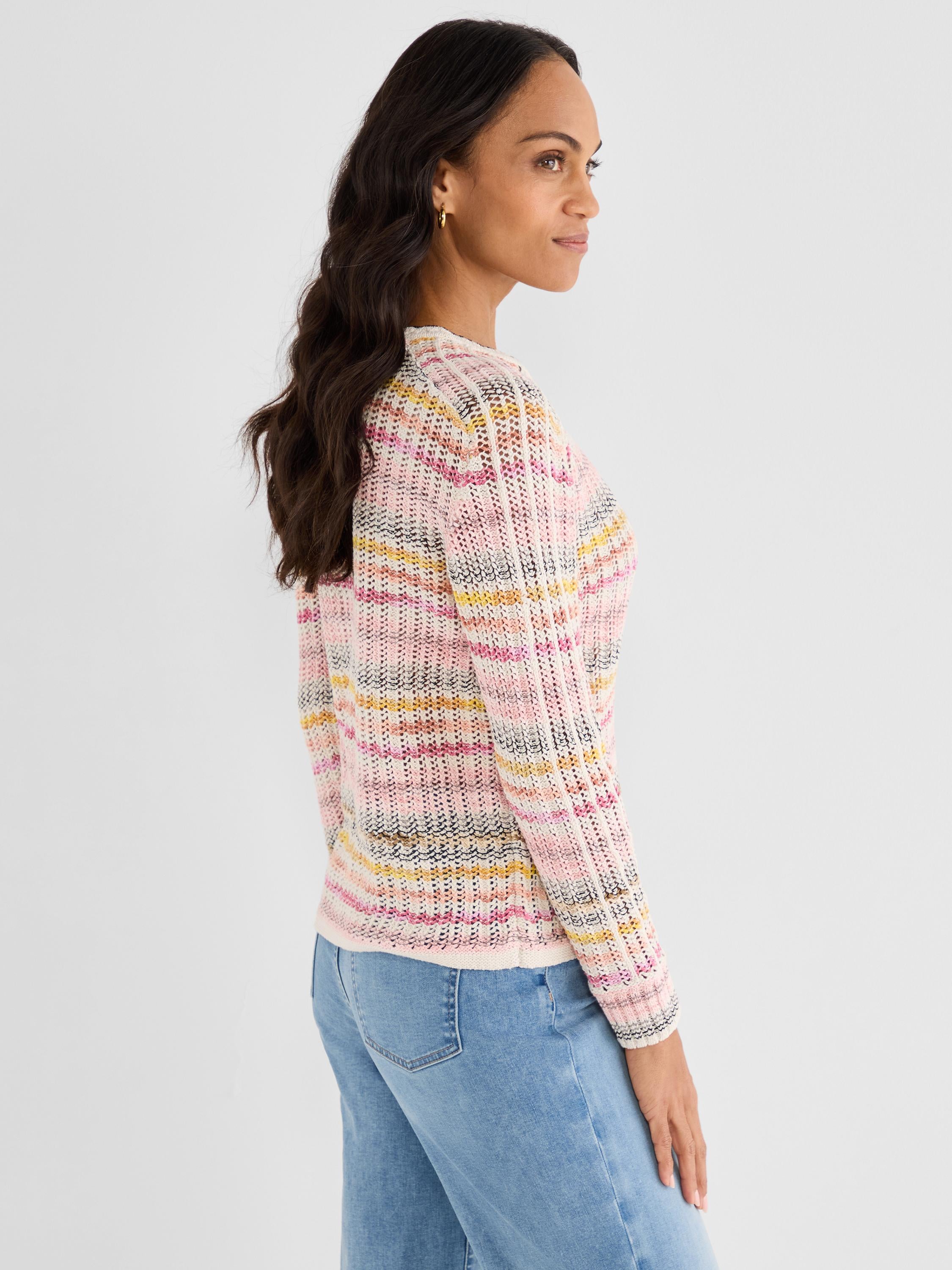 The model wears a slim pink and multicolor striped sweater with an airy, textured open-knit construction.