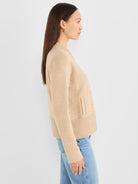 A model wears a structured, fitted beige knit cardigan that features light buttons and a wide ribbed hem.