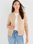 A beige cropped knit cardigan featuring a ribbed collar, button front, and relaxed fit is styled with denim.