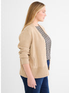 A relaxed button-front tan knit cardigan is worn, featuring a ribbed hem and button detail on the hip pockets.
