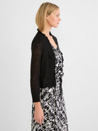 Black cardigan with ruffled trim along the opening and neckline, featuring light, semi-sheer sleeves.
