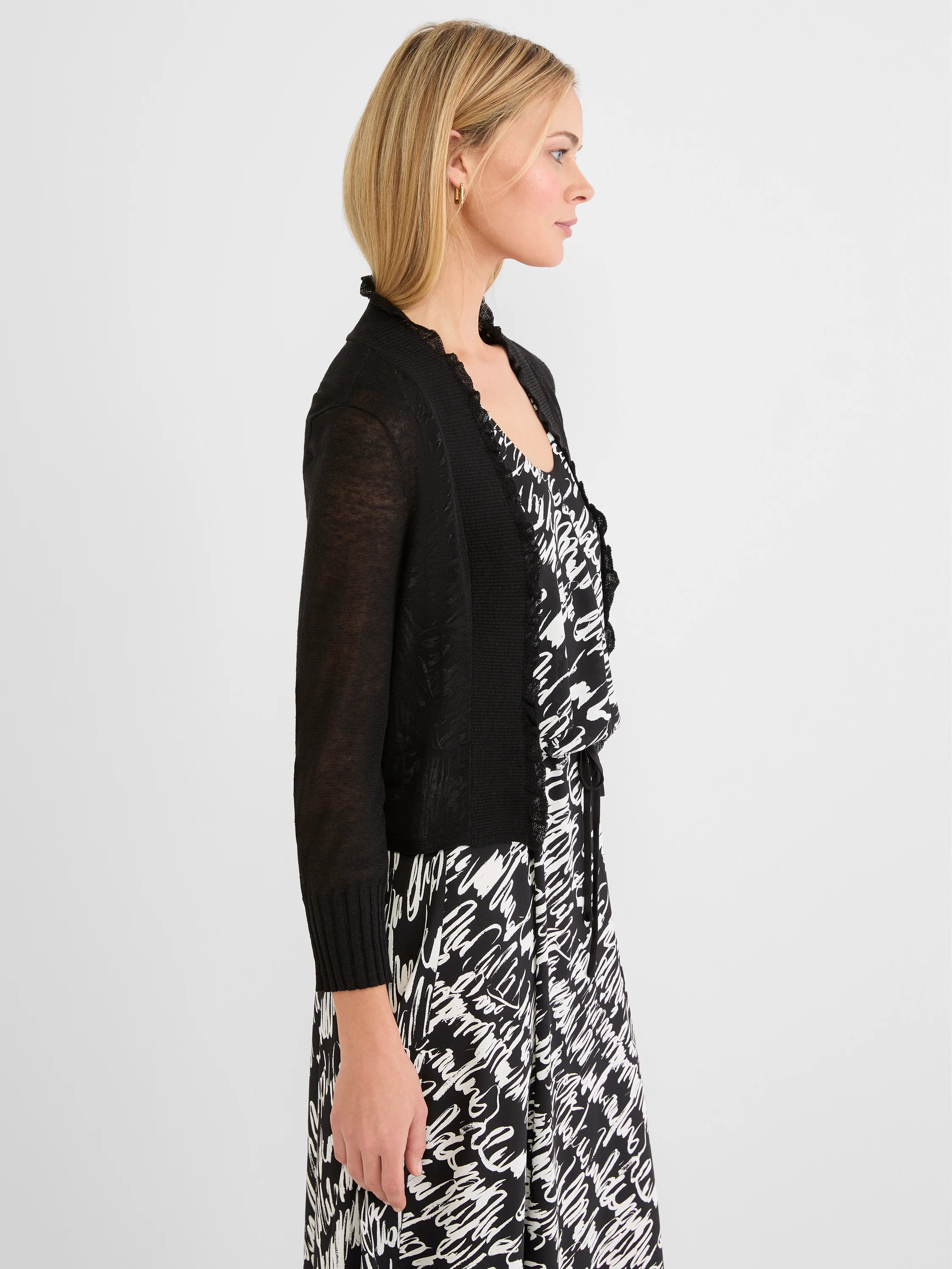 Black cardigan with ruffled trim along the opening and neckline, featuring light, semi-sheer sleeves.