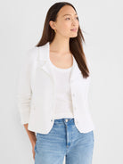 A model wears a white structured knit jacket featuring a lapel collar, button front closure, and patch pockets.