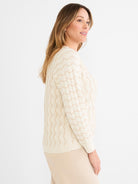 The model wears a relaxed fit ivory and tan knit sweater featuring a wavy open stitch design.