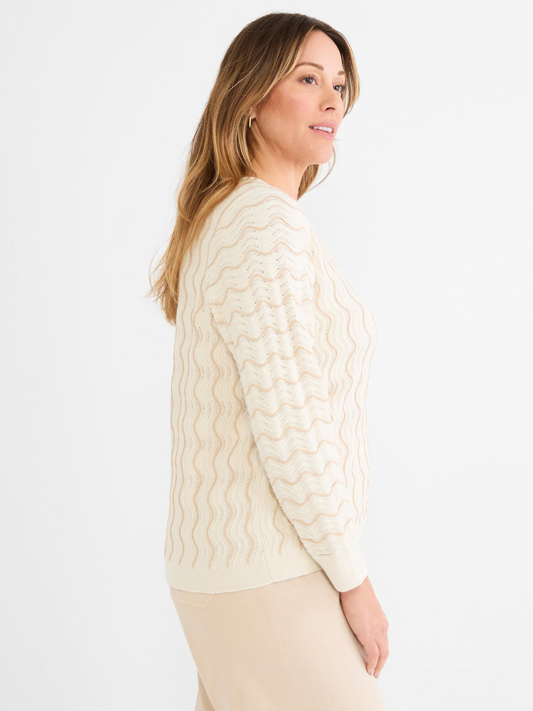 The model wears a relaxed fit ivory and tan knit sweater featuring a wavy open stitch design.