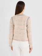The model wears a fitted, collarless, multicolor tweed jacket with geometric trim and a fringed hem.