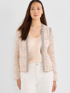 A model wears a light pink speckled tweed jacket featuring ornamental braided trim and a frayed hem.