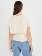 Light beige short-sleeve knit tee with a crew neck and a cropped layered hem showing subtle open knit sleeve detailing.