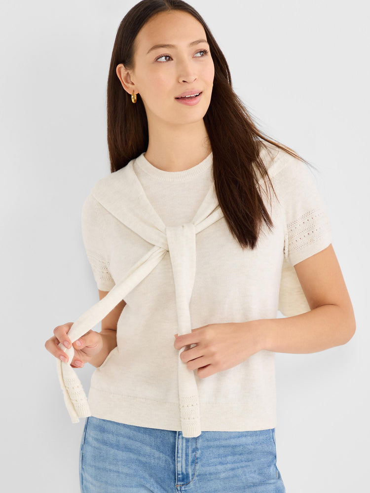 The model wears an oatmeal short-sleeve knit top with subtle eyelet sleeves, casually styled with a matching sweater tied.