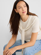 Cream short-sleeve knit top with eyelet cuff detail, styled with a matching sweater tied draped over the neck.